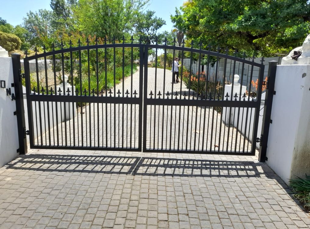 Black steel double swing gate with an arched top between white pillars