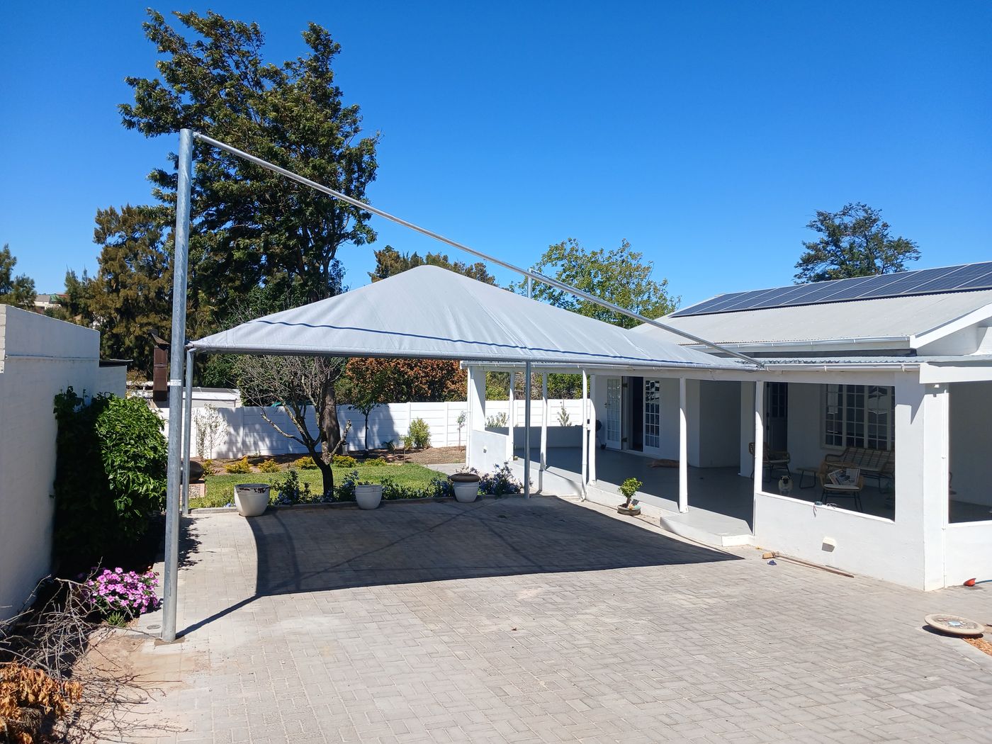 Light grey shade sail port over a paved driveway beside a white house