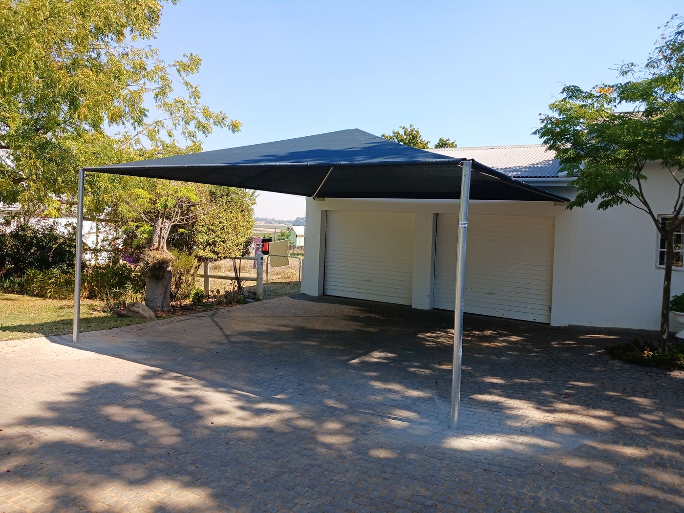Dark shade sail carport on galvanised poles beside a house and garage