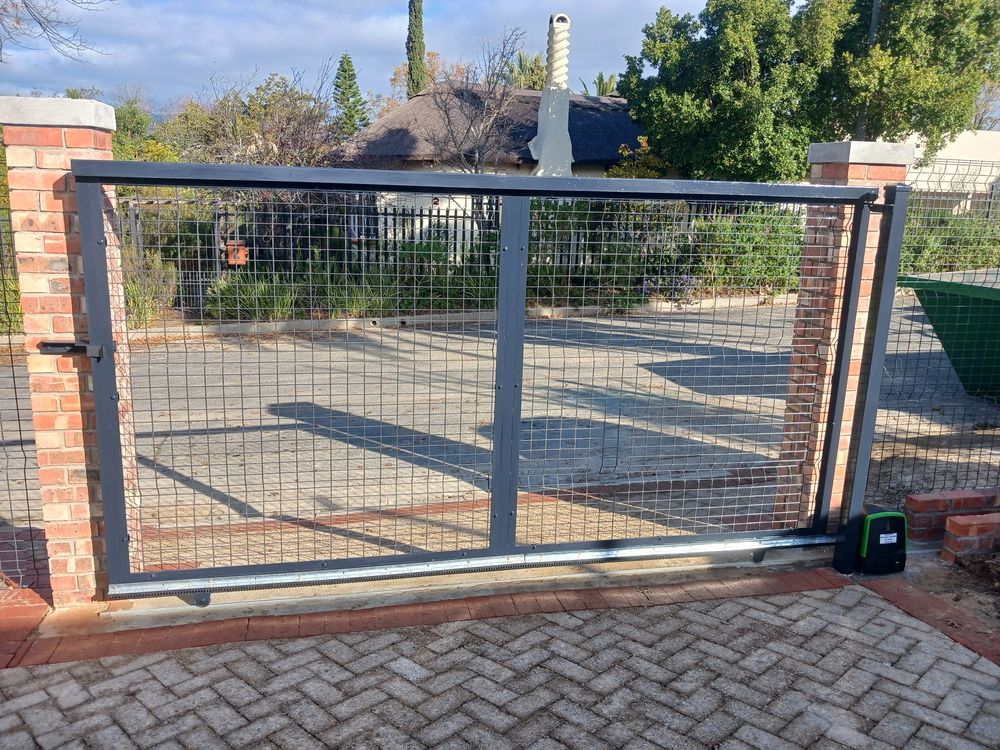 Steel mesh sliding gate between brick pillars with its gate motor at the base