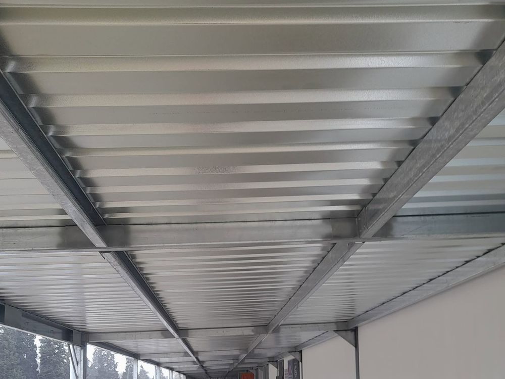Underside of a long galvanised steel carport roof running along a building