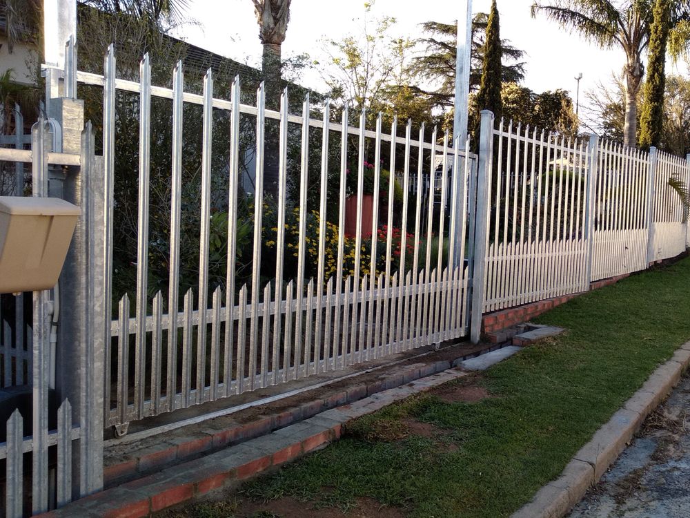 White steel picket fence along a street lined with palm trees