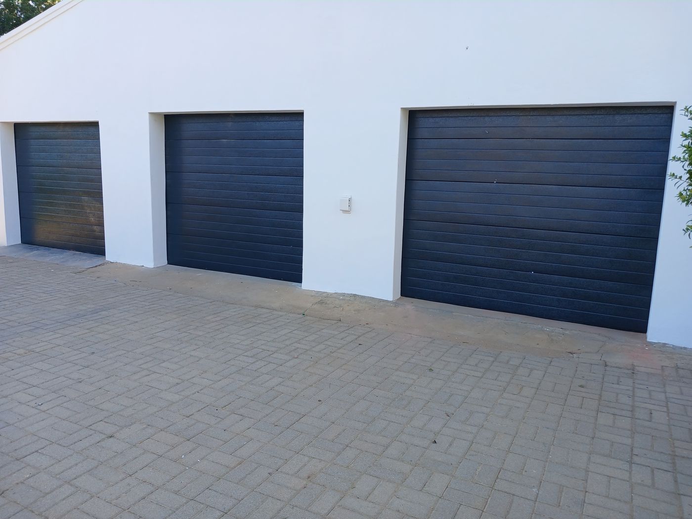 Three dark grey sectional garage doors on a white building