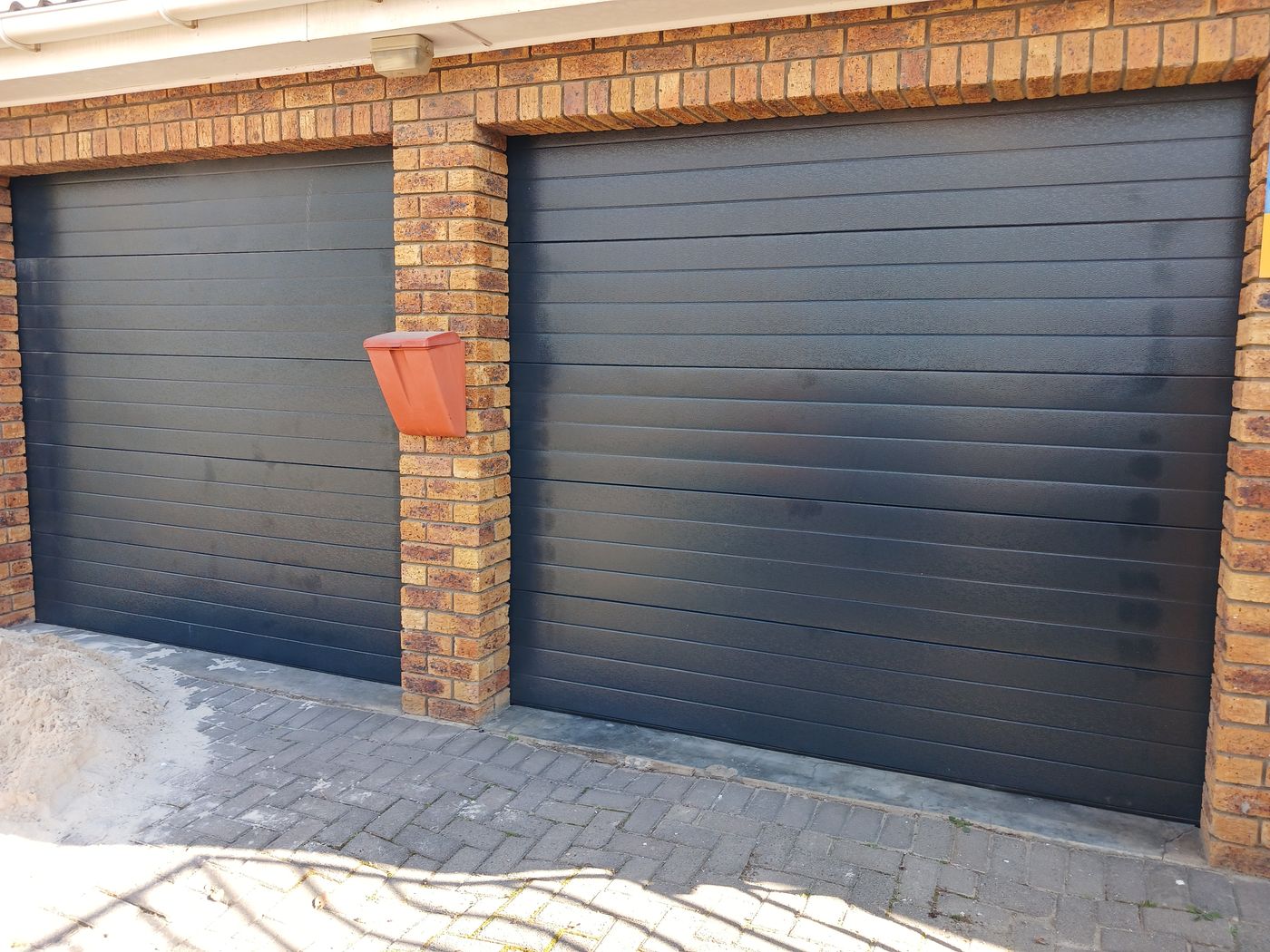 Two charcoal sectional garage doors set into a face-brick wall